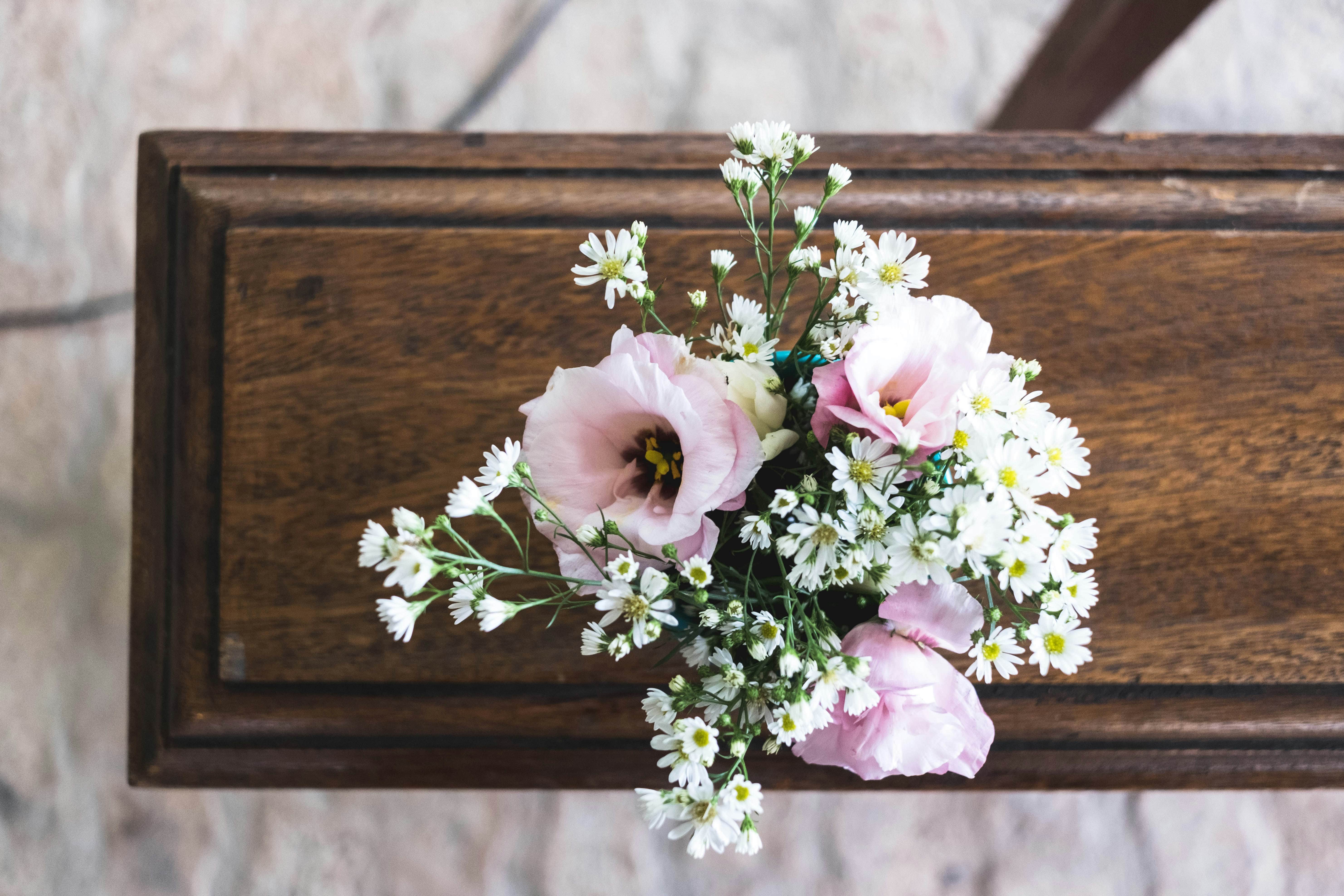 A top-down view of a bouquet with soft pink roses and small white flowers on a wooden surface, evoking a serene and sentimental atmosphere.